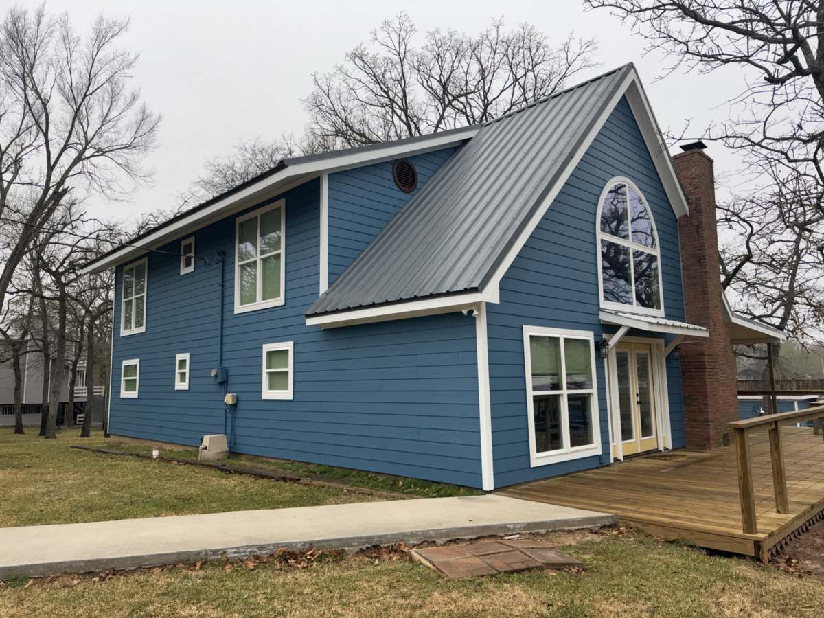 Blue two story home with white trim and a metal roof, freshly painted, in the Brazos Valley, TX
